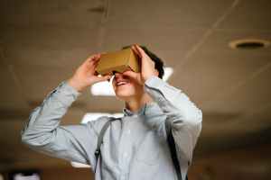 man in grey dress shirt using brown cardboard vr glasses