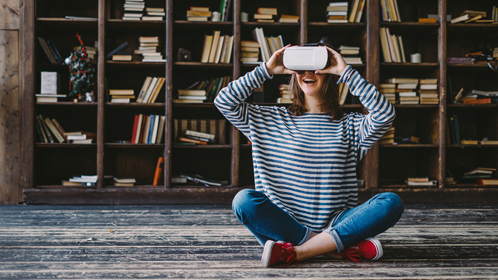 Teenage girl sitting cross-legged on floor using VR goggles.