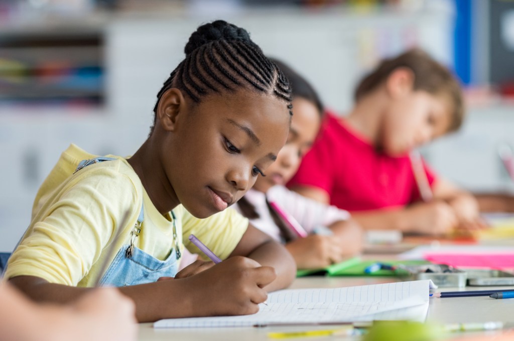 Children writing notes in classroom. 