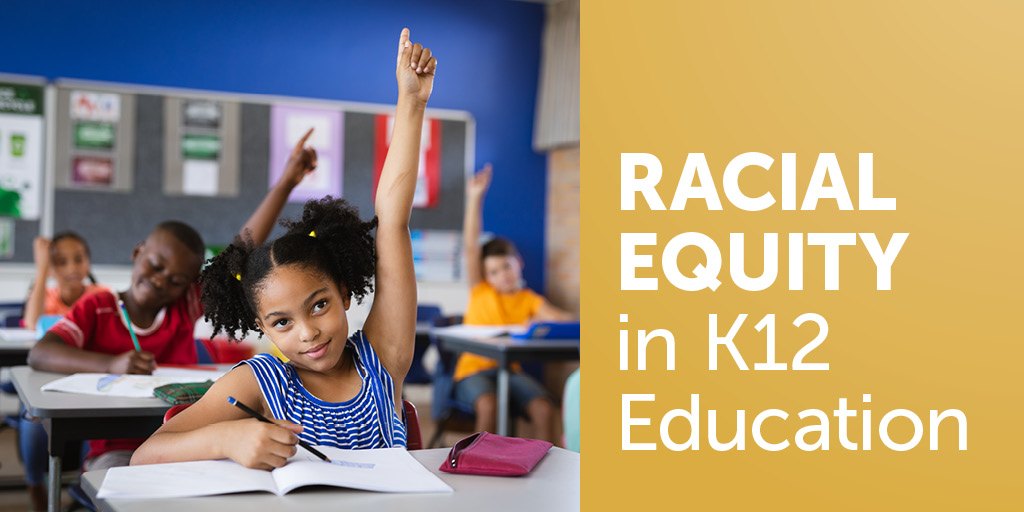 K12 students engaged in the classroom. Kids are sitting at their desks and holding up their hands to answer a question.