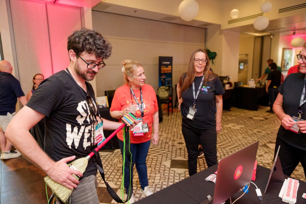 Group of 4 people at a networking event laughing. Man playing broomstick guitar
