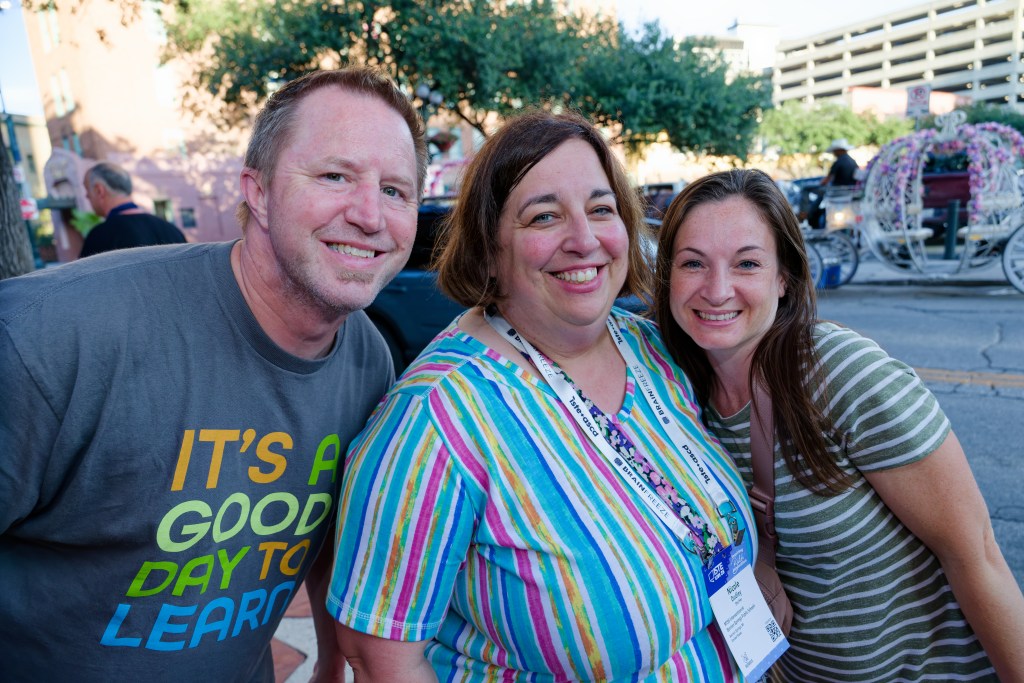 Three colleagues smiling for a photo outdoors while lined up for an event